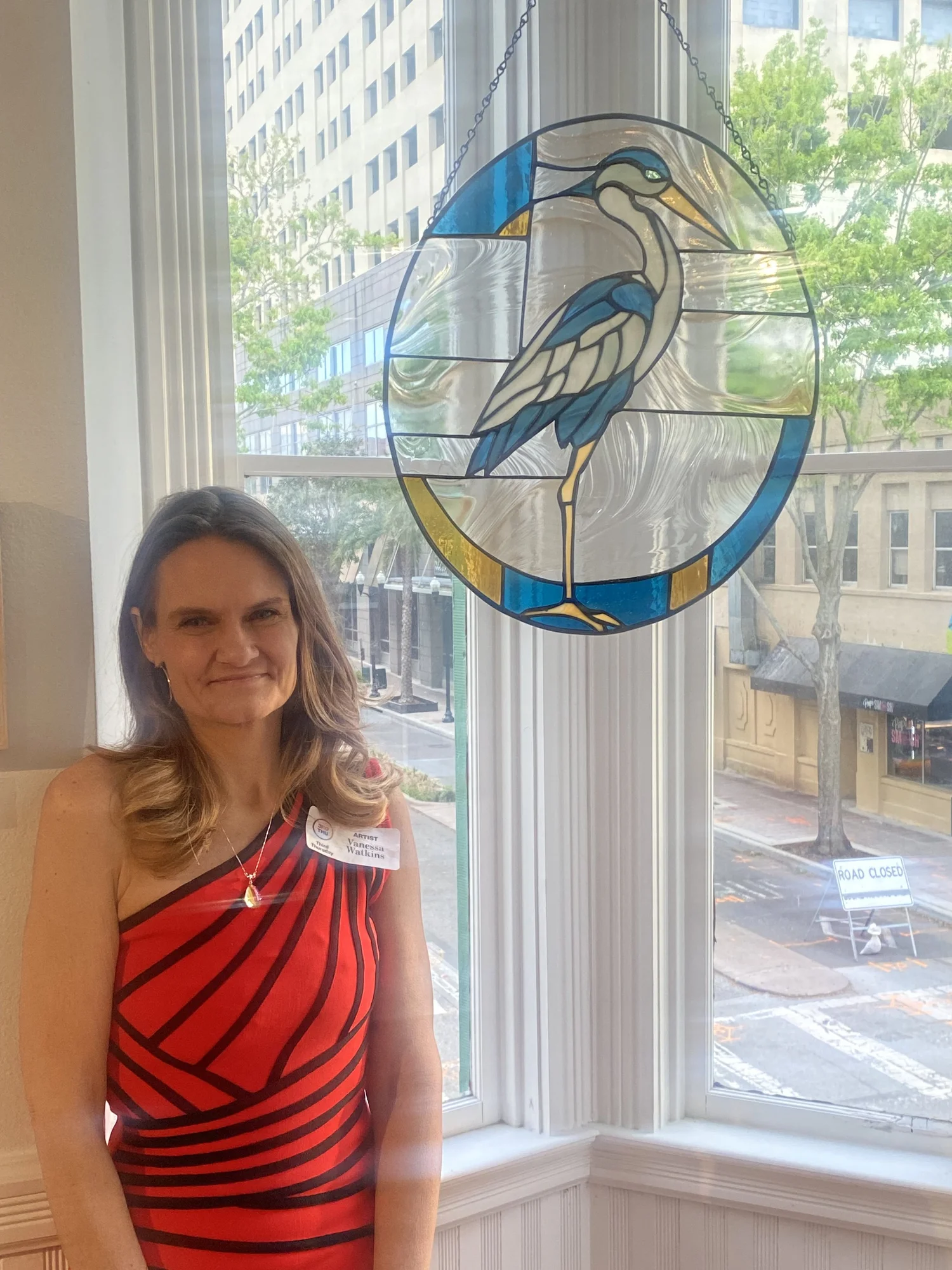Vanessa Watkins beside a blue and clear stained glass heron panel